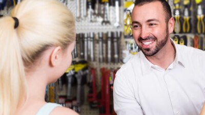 Back of blonde woman's head facing smiling man in dealership.