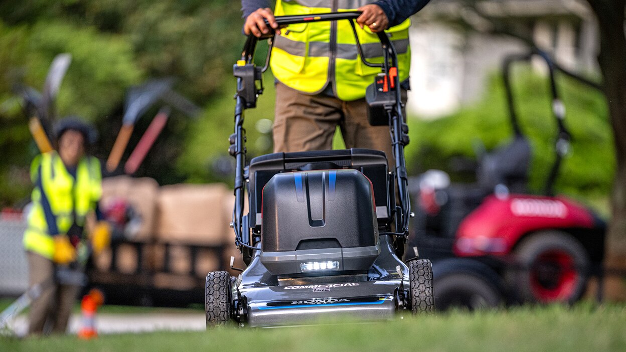 Full frontal view of a person pushing a battery lawn mower in the lawn. 