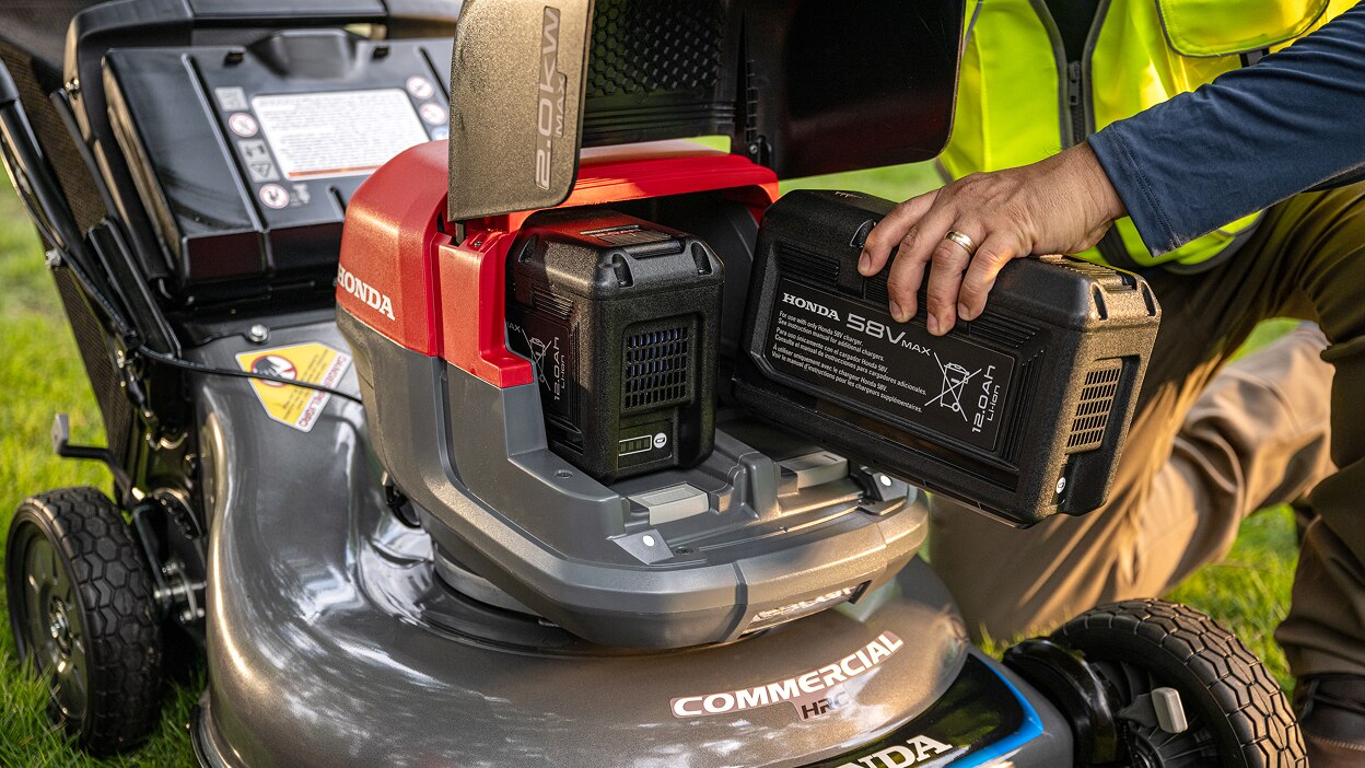 Close up showing the user inserting the battery into the battery lawn mower battery bay.
