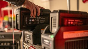 A person placing battery lawn mower battery on its charger in the garage with a second battery in the foreground. 