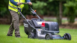 View from three-quarter front right showing a worker pushing a battery lawn mower on the lawn. 