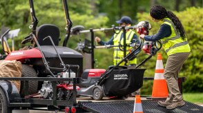 Worker unloading a battery lawn mower from a trailer. 