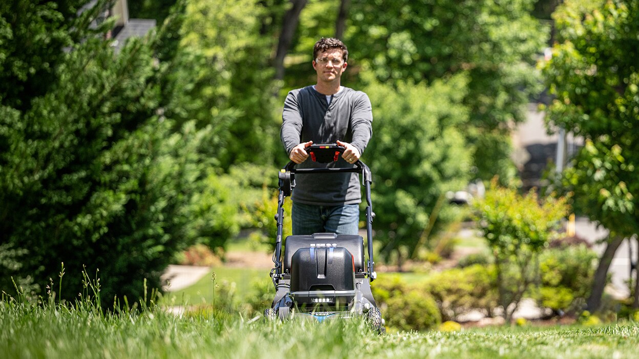 Full frontal view of a person pushing a battery lawn mower in the lawn.