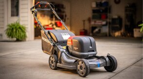 Image of a battery lawn mower in front of an open garage door. 