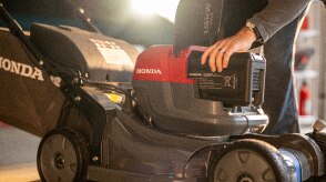 Close up showing the use inserting the battery into the battery lawn mower battery bay. 