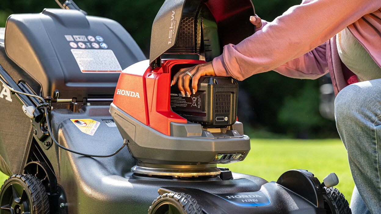 Close up showing the use inserting the battery into the battery lawn mower battery bay.