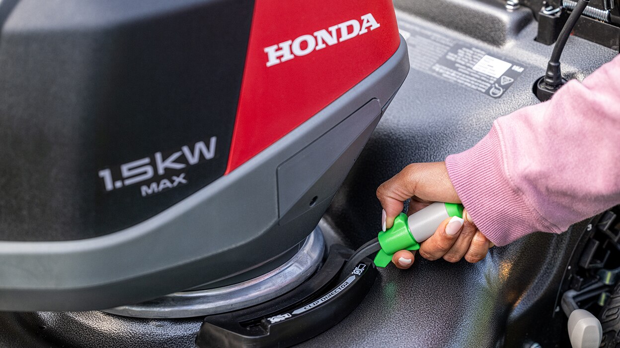Close up of a person's hand adjusting the blade height using the lever on the top of the lawn mower.