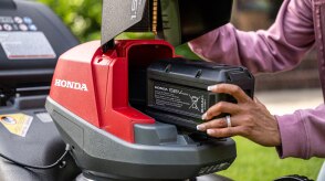 Close up showing the use inserting the battery into the battery lawn mower battery bay. 