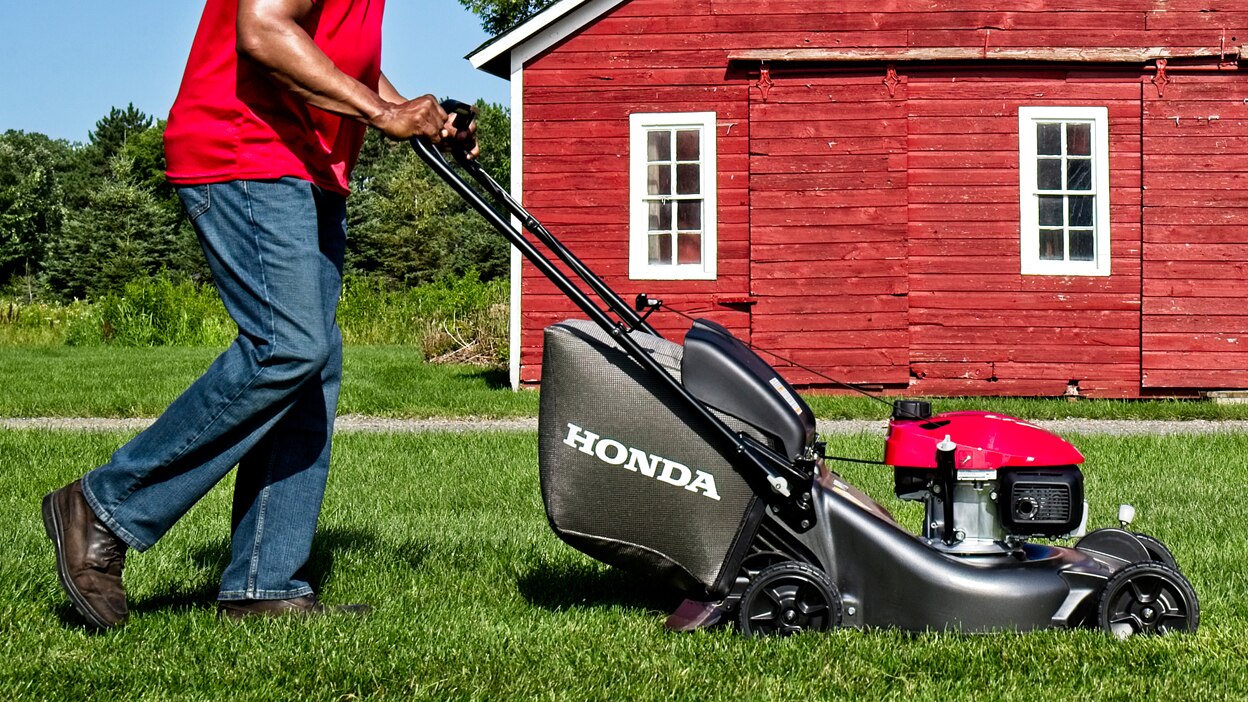 Personne tondant la pelouse, direction droite. Grange rouge en arrière-plan.