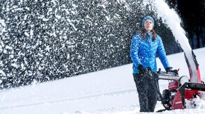Wide view of a woman pushing a snowblower and clearing snow.  